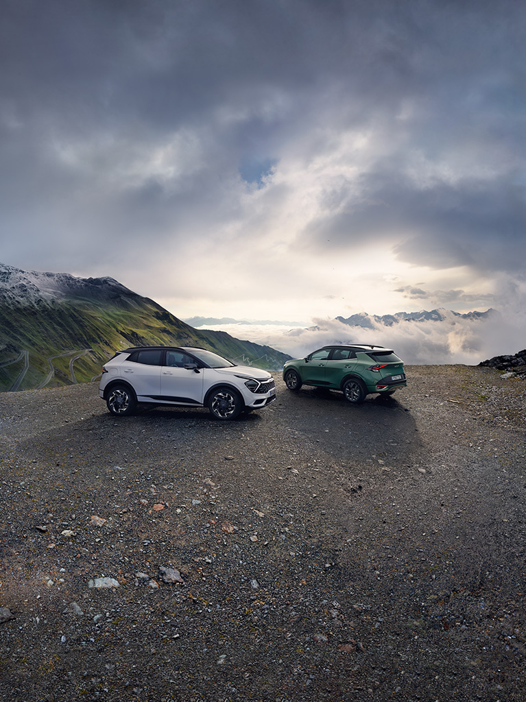 Zwei Sportage stehen auf einem Parkplatz vor Berggipfeln